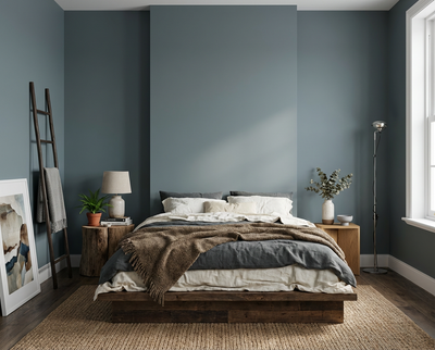Ein minimalistisches Bett aus Holz steht zentral vor einer Wand in Fjord Mist, einer kühl wirkenden graublauen Wandfarbe, realisiert mit der re-box Renovierungsbox.